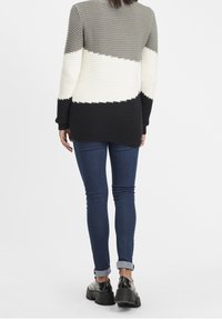 Strickpullover mit geometrischem Design in Grau, Weiß und Schwarz; verfügt über strukturierte Streifen und wird mit dunklen Jeans und klobigen schwarzen Schuhen kombiniert.