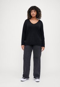 Black long-sleeve top with a V-neck, paired with dark gray wide-leg pants and white sneakers. Fabric appears soft with a relaxed fit.