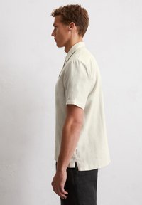 Kurzarm-Hemden aus Leinen in hellem Beige mit Kragen, entspannter Passform und seitlichen Schlitzen für Bewegungsfreiheit.
