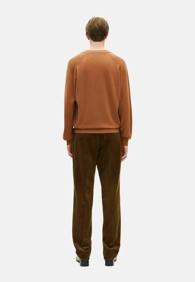 Brauner Pullover mit gerippten Bündchen, kombiniert mit dunkelgrünen Cordhosen, die einen entspannten Schnitt haben, und einer Rückansicht des Kleidungsstücks.