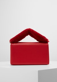 Červená kožená kabelka s texturovanou červenou umělou kožešinou na rukojeti. Obdélníkový tvar, hladký povrch a minimalistický design. Žádné viditelné kovové části.