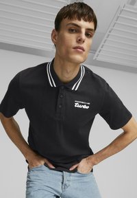 Svart poloskjorte med hvitstripet krage og "Porsche Turbo" logo i hvitt. Brukes sammen med lyseblå jeans, med en tett passform.