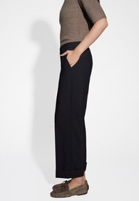 Black, loose-fitting trousers with side pockets, cuffed hems, and a smooth, textured fabric. Paired with brown shoes.