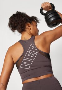 Top desportivo castanho escuro com detalhes em rede, apresentando um grande texto branco "NER" de um lado. O design nas costas inclui estilo de corredor para maior mobilidade.