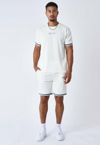 Camiseta blanca de manga corta con textura acanalada y rayas azules, combinada con pantalones cortos a juego que presentan un logo y dobladillos a rayas.