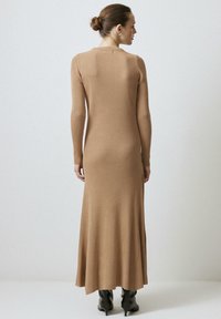 Pikk, ribadest kangast, kameli värvi kleit pika varrukaga. Omab istuvat ülaosa ja laienevat hemmi, koos mustade kontsadega saabastega.