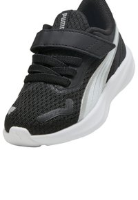 Scarpa sportiva nera con tessuto a rete, collare imbottito e cinturino in Velcro. Suola bianca con dettagli testurizzati e una striscia riflettente argento.