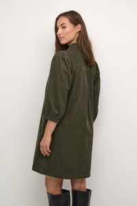 Olíva zöld kordbársony ruha galléros nyakkal, puffos ujjal és laza fazonnal. A ruha hátán ráncolás található, és térdig érő hosszúságú.