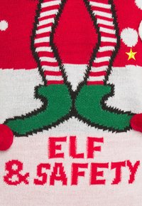 Piernas de elfo con medias a rayas rojas y blancas y zapatos verdes sobre el texto rojo "ELF & SAFETY" en una tela de punto festiva.