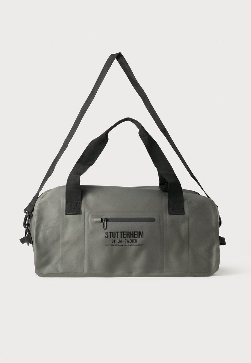 Vihreä vedenkestävä reppulaukku mustalla vetoketjutaskulla, tukevilla hihnoilla ja yksinkertaisella logolla sivussa. Tasaista rakennetta, pyöreä muoto.