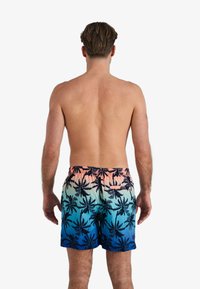 Shorts de bain avec une taille élastique, affichant un dégradé de rose à bleu, ornés de motifs de feuilles de palmier noires.
