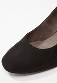 Gros plan sur l'avant d'une chaussure plate pour femme en daim noir, avec un bout rond et une doublure intérieure douce.