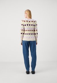 Maglione lavorato a maglia con una palette di colori pastello e motivi a cuore, maniche lunghe e orlo a coste. Abbinato a jeans blu dal taglio morbido.