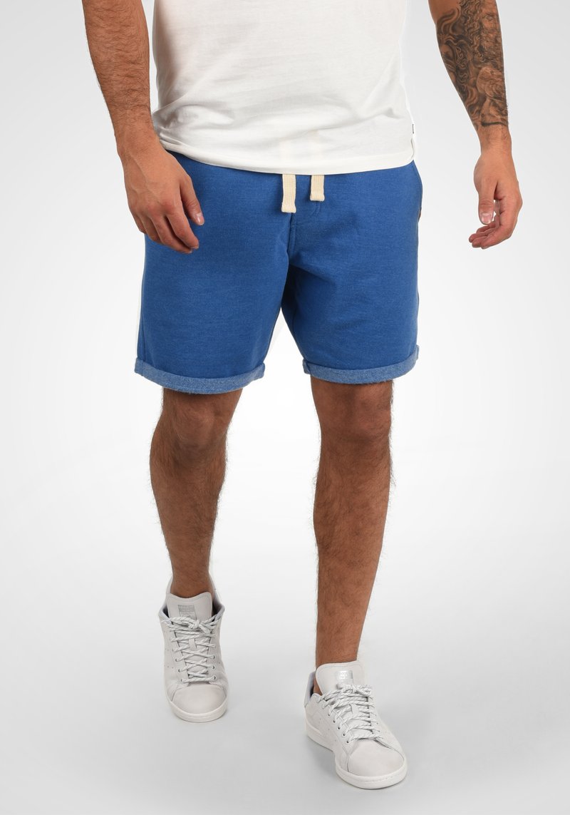 Blå sweat shorts med rullekanter, strikket midje med snor og en myk tekstur, kombinert med hvite høy-hæl sneakers.
