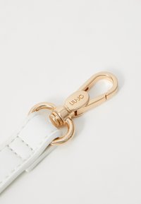 Witte leren band met een gouden sluiting, voorzien van een ronde ring en een geperst logo. Soepele textuur en nette stiksels.