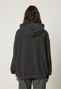 Felpa oversize nera con un tessuto testurizzato, dotata di cappuccio con cordoncino e polsini a costine. Vestibilità ampia, design minimalista senza decorazioni.
