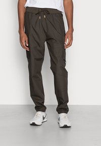 Leichte Cargo-Hose in dunklem Olivgrün, mit elastischem Bund und Kordelzug, mehreren Taschen und einer glatten, matten Oberfläche.