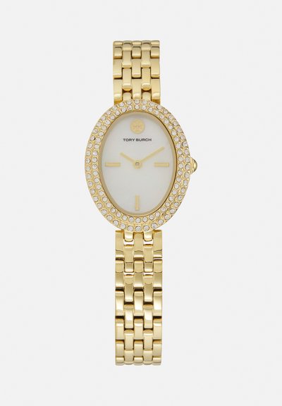 Tory Burch polshorloge in goudkleur met ovale kristalversierde lunette, witte wijzerplaat, gouden markers en metalen schakelarmband.