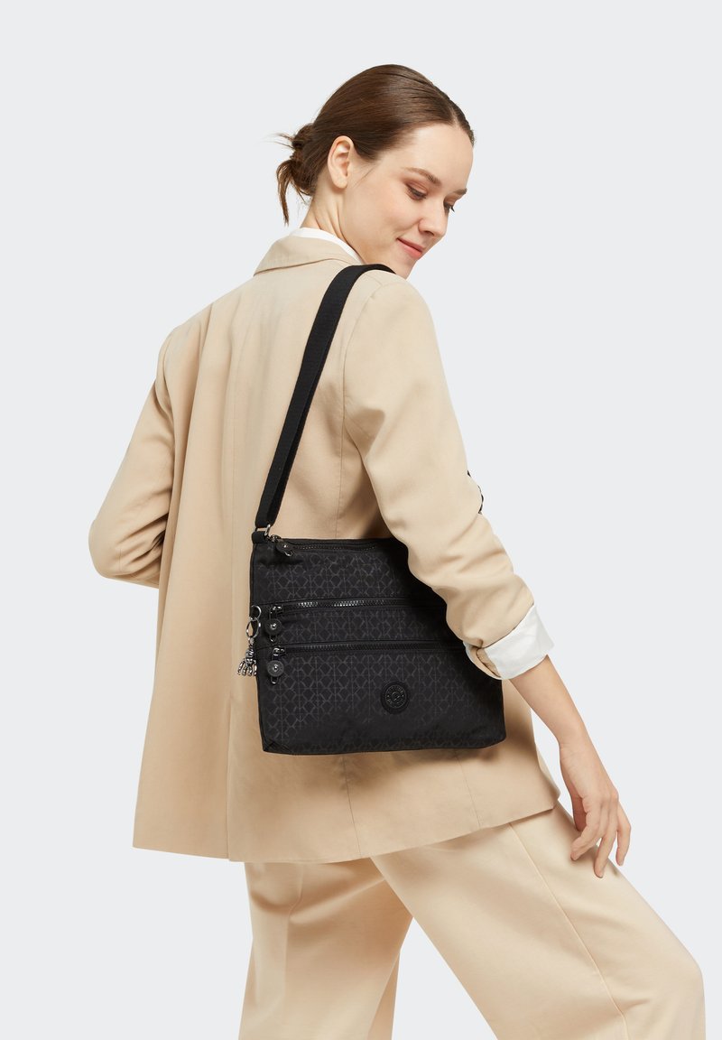Black fabric crossbody bag featuring three zippered compartments and a logo accent. The strap is adjustable for comfort.