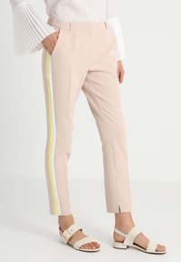 Light pink tailored trousers with side yellow and white stripes, featuring a slim fit and slits at the ankles, paired with flat sandals.
