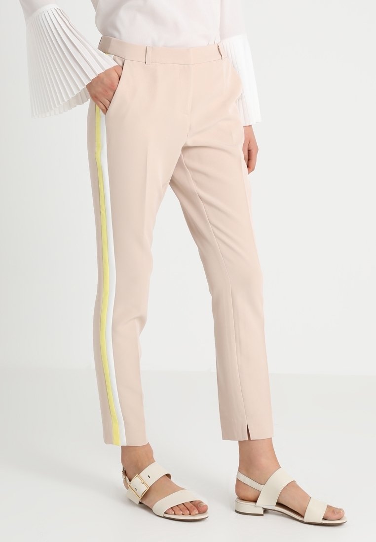 Light pink tailored trousers with side yellow and white stripes, featuring a slim fit and slits at the ankles, paired with flat sandals.
