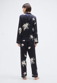 Ensemble de pyjama à fleurs bleu marine en tissu doux, comprenant une chemise boutonnée à manches longues et un pantalon à jambes larges avec passepoil blanc et motifs floraux détaillés.