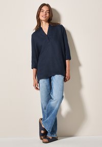 Tunica di lino blu navy con scollatura a V e maniche a tre quarti, abbinata a jeans di denim blu chiaro e sandali navy con suola in sughero.