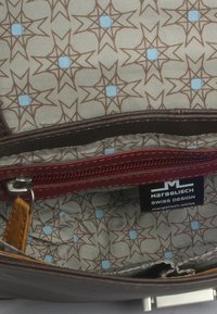 Interno di una borsa in pelle marrone con una fodera a motivo che presenta accenti blu a forma di stella, tasca con zip e etichetta del marchio.