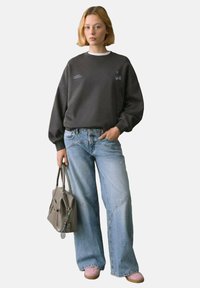 Grauer Sweatshirt mit Kirschgrafik, lässiger Schnitt. Hellblaue weit geschnittene Jeans, hellrosa Schuhe und eine graue Handtasche. Minimalistische Hardware-Accessoires.