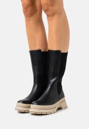 Bottes en cuir noir avec une semelle beige épaisse et des panneaux latéraux élastiques. Le design présente une forme épurée et une tige texturée.