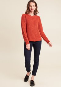 Maglione rosso lavorato a maglia con motivo testurizzato, maniche lunghe e colletto rotondo. Abbinato a pantaloni aderenti blu scuro e scarpe slip-on nere.