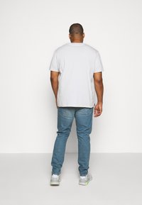 White cotton t-shirt, blue denim jeans, gray and neon sneakers. Plain design with no visible text or patterns, viewed from the back.