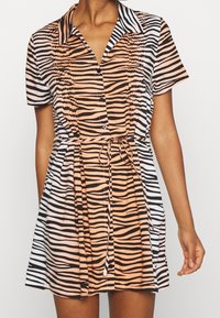 Šaty s krátkým rukávem, které kombinují černé a oranžové pruhy zebry, zapínání na knoflíky vpředu a zavazovací pásek v pase pro přizpůsobený vzhled.