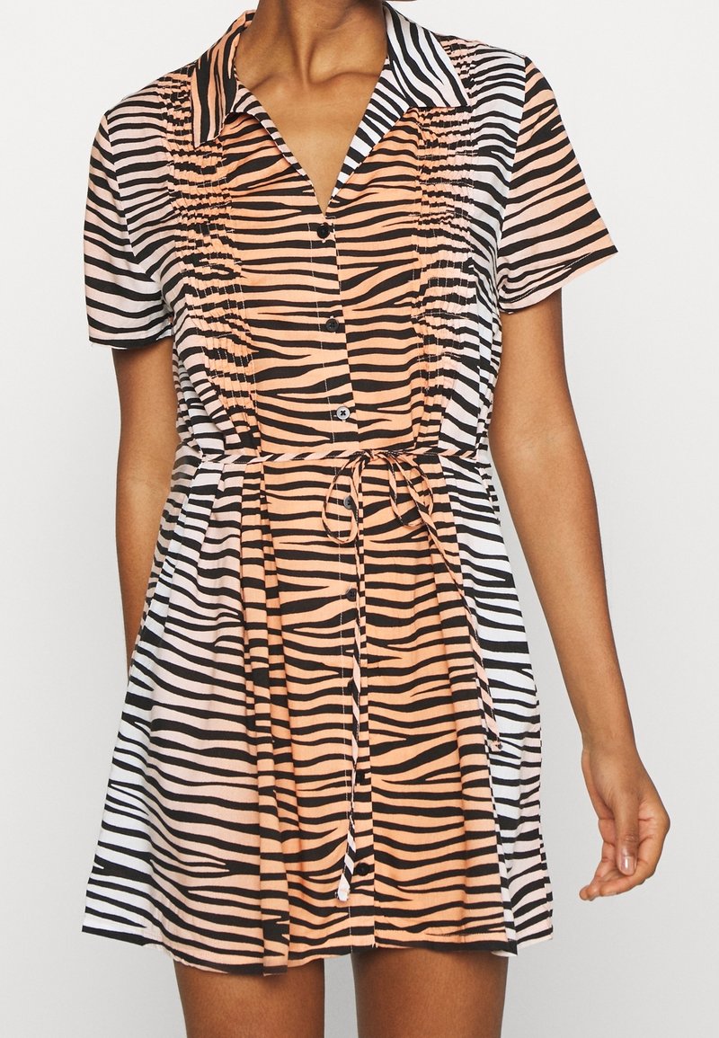 Šaty s krátkým rukávem, které kombinují černé a oranžové pruhy zebry, zapínání na knoflíky vpředu a zavazovací pásek v pase pro přizpůsobený vzhled.