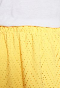 Geel rokje met een gestructureerd patroon, voorzien van zigzagontwerpen en kleine uitsparingen. Elastische tailleband voor een goede pasvorm. Gecombineerd met een witte top.