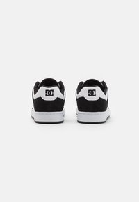 Black and white sneakers featuring a suede upper, padded collar, and a white rubber sole. DC logo visible on the heel and side.