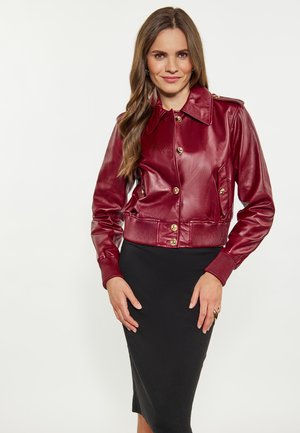 Piros bőr röviddzseki, kivágott gallérral, arany gombokkal és bordás mandzsettákkal, egy Testre simuló fekete szoknyával párosítva.