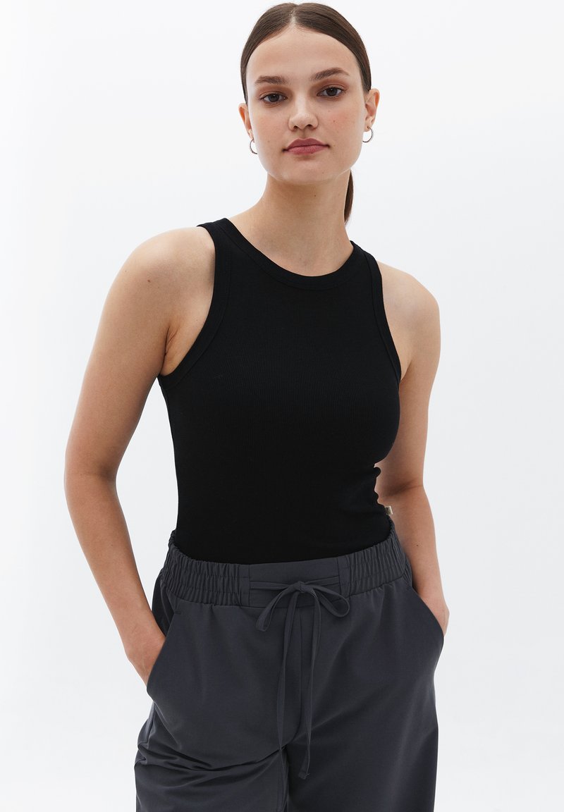 Top sin mangas de rayas negras con cuello redondo, combinado con pantalones de chándal grises con cordón que cuentan con una cinturilla elástica y bolsillos laterales.