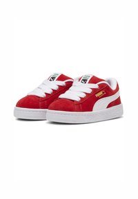 Tenisi roșii din suede cu șireturi albe și talpă din cauciuc. Dungi laterale albe și branding pe limbă. Design clasic low-top.