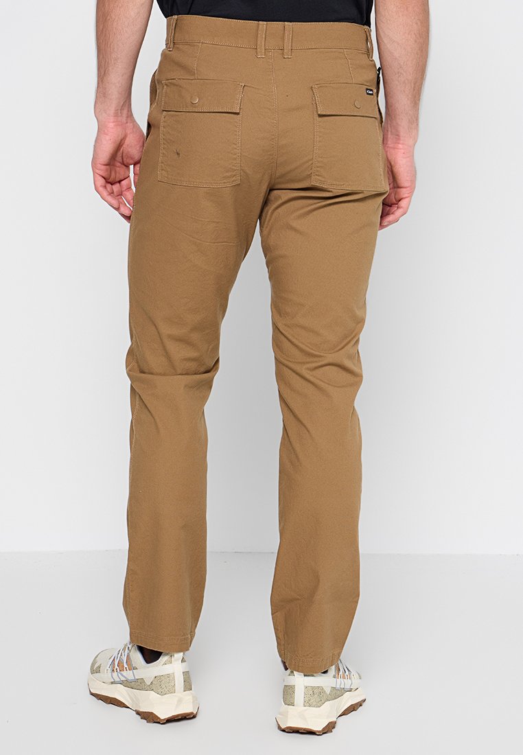 Pantalones cargo color beige con un diseño ajustado, que cuentan con dos bolsillos traseros, una textura suave, y combinados con zapatillas deportivas de color claro.