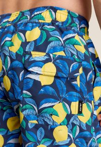 Shorts de bain en tissu bleu marine avec un motif de citrons et de feuilles. Comprend une poche arrière avec une fermeture à pression et une étiquette de marque.