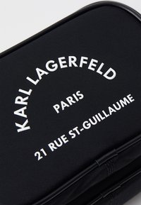 Borsa nera texturizzata con testo bianco in rilievo: "KARL LAGERFELD," "PARIS," e "21 RUE ST-GUILLAUME," con angoli arrotondati.