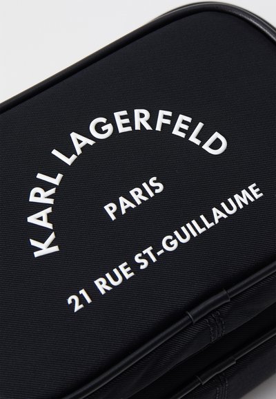 Sac noir texturé avec texte en relief blanc : "KARL LAGERFELD," "PARIS," et "21 RUE ST-GUILLAUME," avec des coins arrondis.
