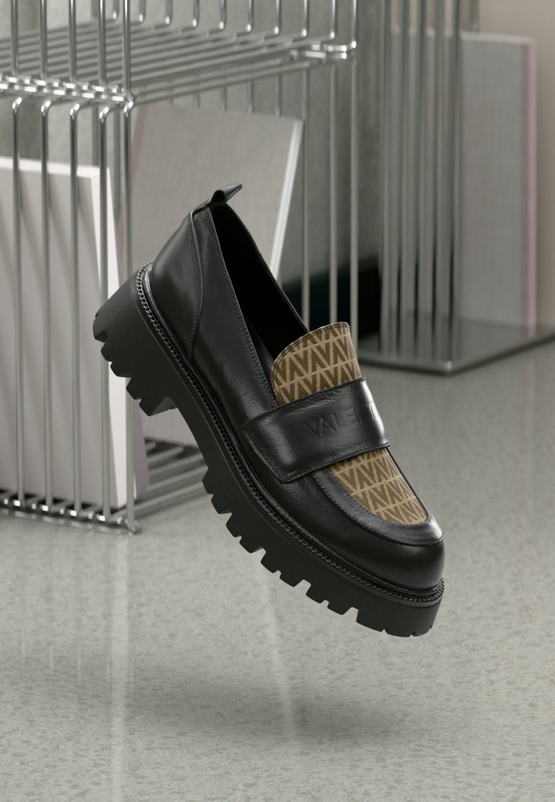 Mocassins en cuir noir avec un panneau textile marron à motifs, semelle en caoutchouc noir épaisse et une sangle étiquetée "VALENTINO". Détails de surface texturés visibles.