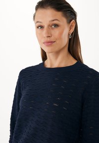 Námořnický modrý pletený svetr s texturovaným vlnitým vzorem a žebrovaným výstřihem. Lehký design s jemnými otvory pro prodyšnost.