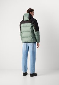 Gewatteerde jas in mintgroen met zwarte schouders en capuchon, met een rechte snit en een gestructureerd oppervlak. Gecombineerd met lichtblauwe jeans.