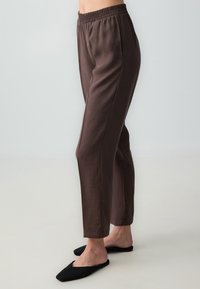 Lichte, bruine, elastische broek met rechte benen; gecombineerd met zwarte, platte instapschoenen. Glad textuur, minimalistisch ontwerp.