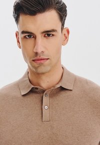 Brązowa koszulka polo z miękkiego materiału, z kołnierzykiem i zapięciem na dwa guziki. Gładka tekstura i dopasowany krój.