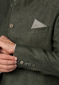 Green textured blazer with wooden buttons and a striped pocket square. Close-up shows a fitted design and detailed stitching on the sleeve.
