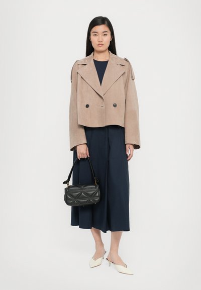 Veste en daim beige cropped avec des manches larges et des boutons double boutonnage, associée à un pantalon marin à jambes larges et à un sac à main noir matelassé.